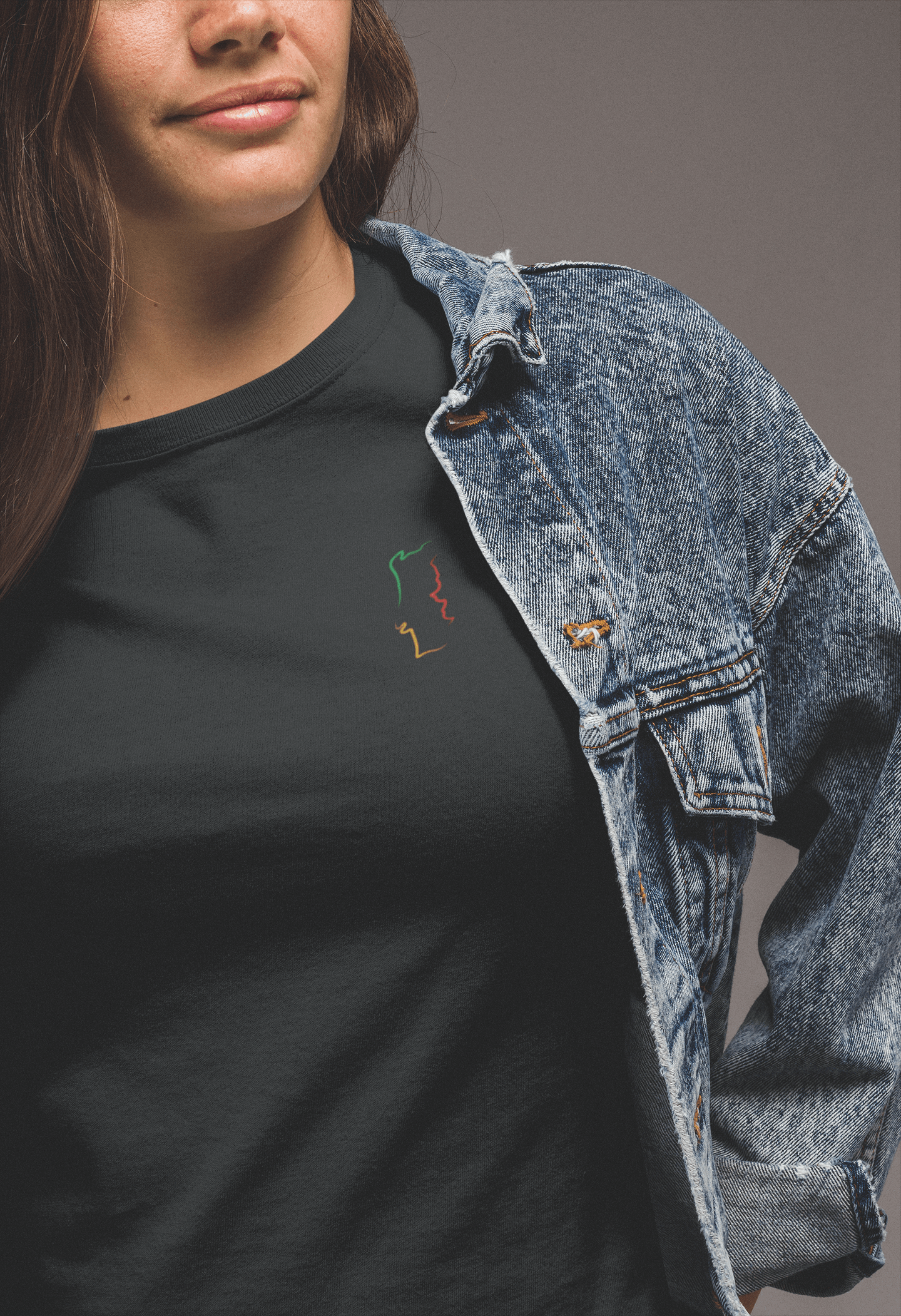 Woman wearing a black Portugal T-Shirt under a denim jacket, featuring a minimalist embroidered map design on organic cotton fabric for a trendy look.