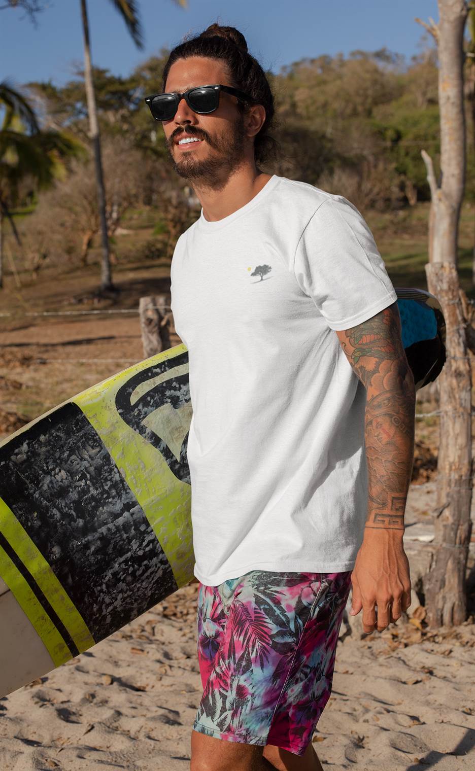 Surfer wearing a white organic T-shirt with a minimalist oak tree and sunset design, paired with tropical shorts. Perfect for beach and casual wear.