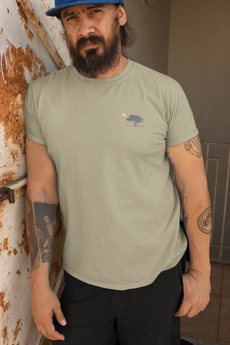 Bearded man wearing a sage green organic T-shirt with a minimalist oak tree and sunset design. A comfortable and sustainable fashion choice.