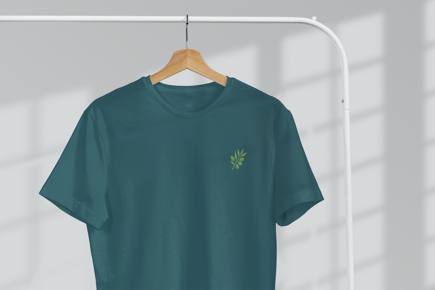 Teal t-shirt with a small green logo on a hanger against a white background