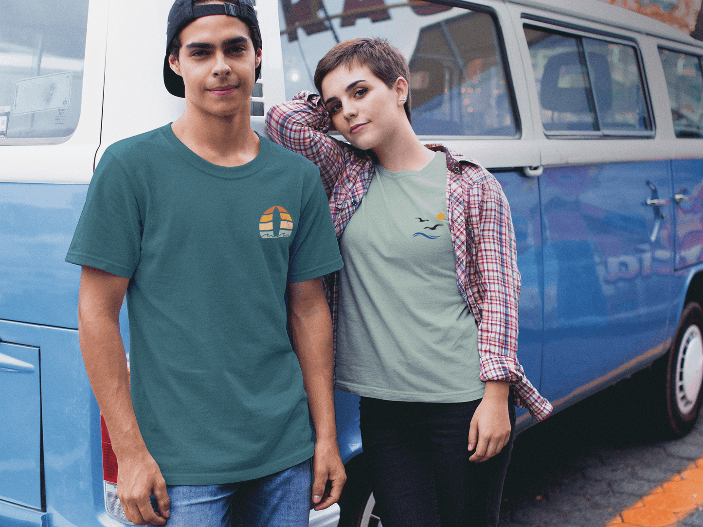 Man in a teal Nazare Surf Minimal Organic T-shirt with a vintage surf logo, standing next to a woman in a casual outfit by a retro van. Unisex and eco-friendly.