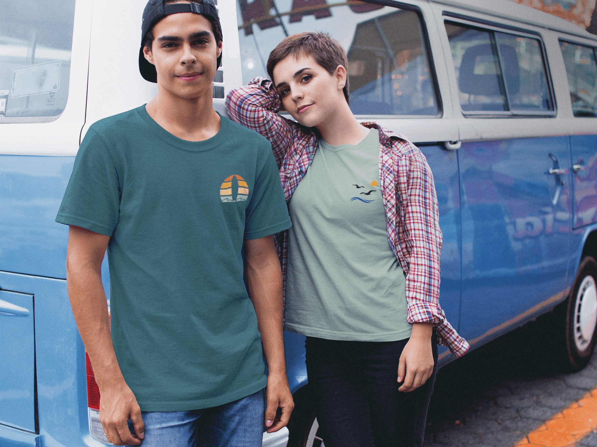 Man in a teal Nazare Surf Minimal Organic T-shirt with a vintage surf logo, standing next to a woman in a casual outfit by a retro van. Unisex and eco-friendly.
