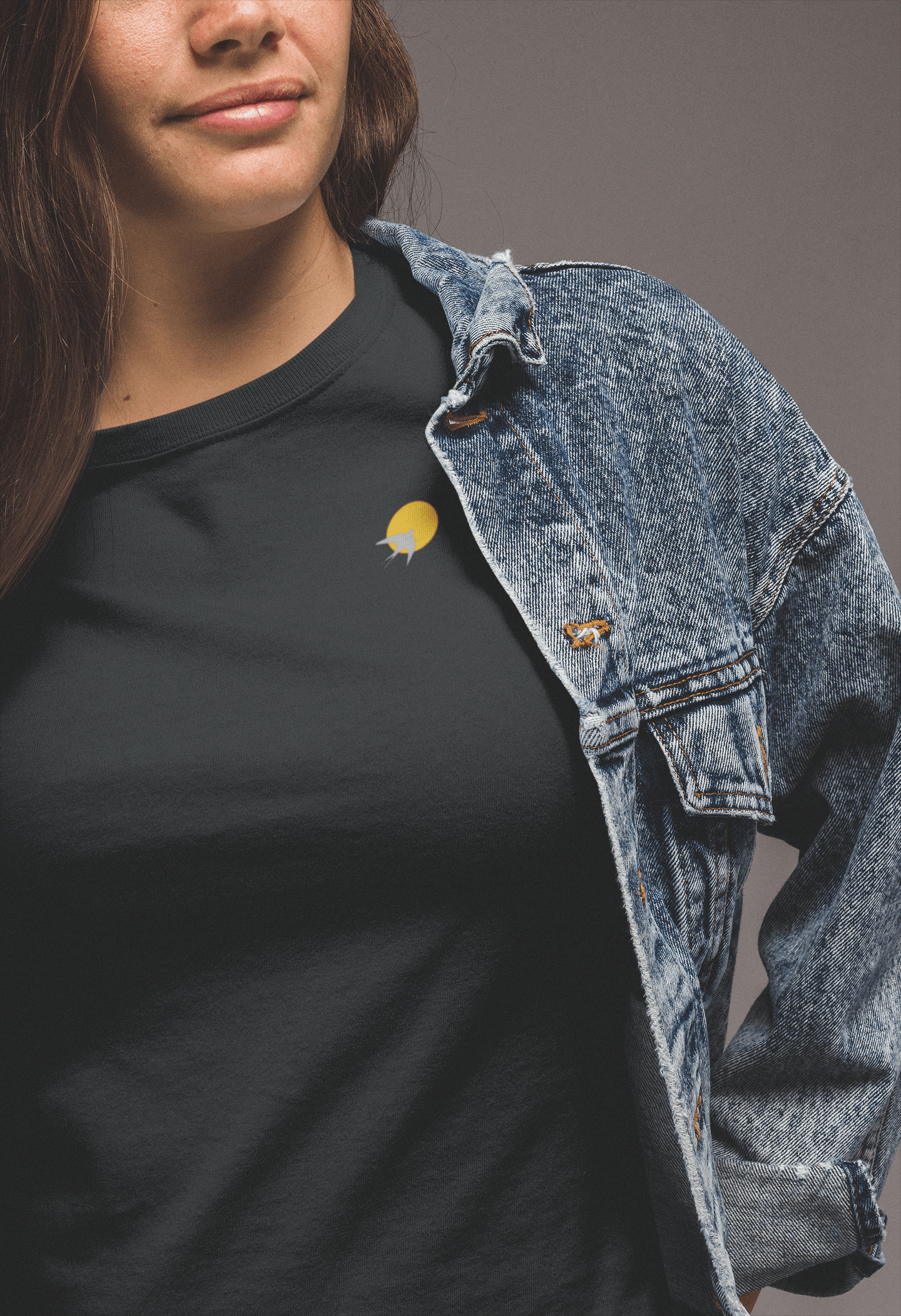 Black Andorinha T-Shirt with a small yellow sun and swallow logo, styled with a denim jacket. A unisex organic cotton tee with a minimalist design.