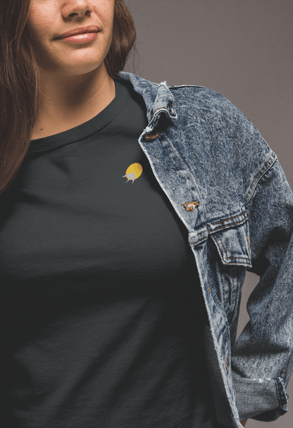 Black Andorinha T-Shirt with a small yellow sun and swallow logo, styled with a denim jacket. A unisex organic cotton tee with a minimalist design.