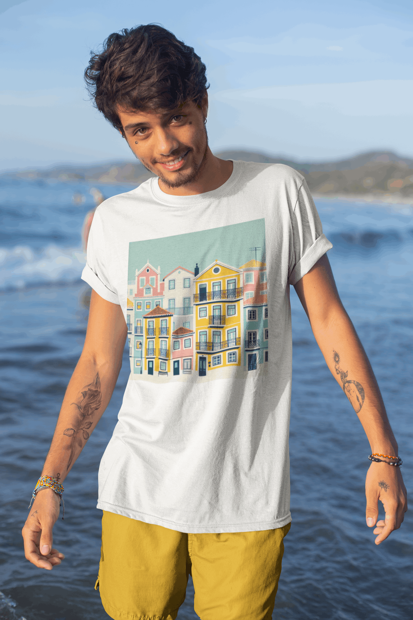 Man wearing a white organic cotton T-shirt featuring Lisbon Alfama houses design at the beach. A sustainable and stylish unisex fashion choice.