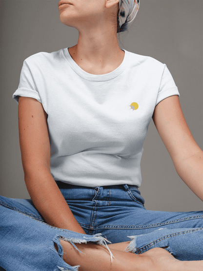 White Andorinha T-Shirt with a subtle swallow and sun logo, paired with ripped jeans. A unisex organic cotton tee with a minimalist aesthetic.