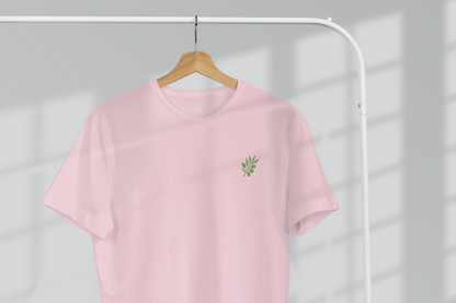 Pink t-shirt with a small green logo on a hanger against a light gray background