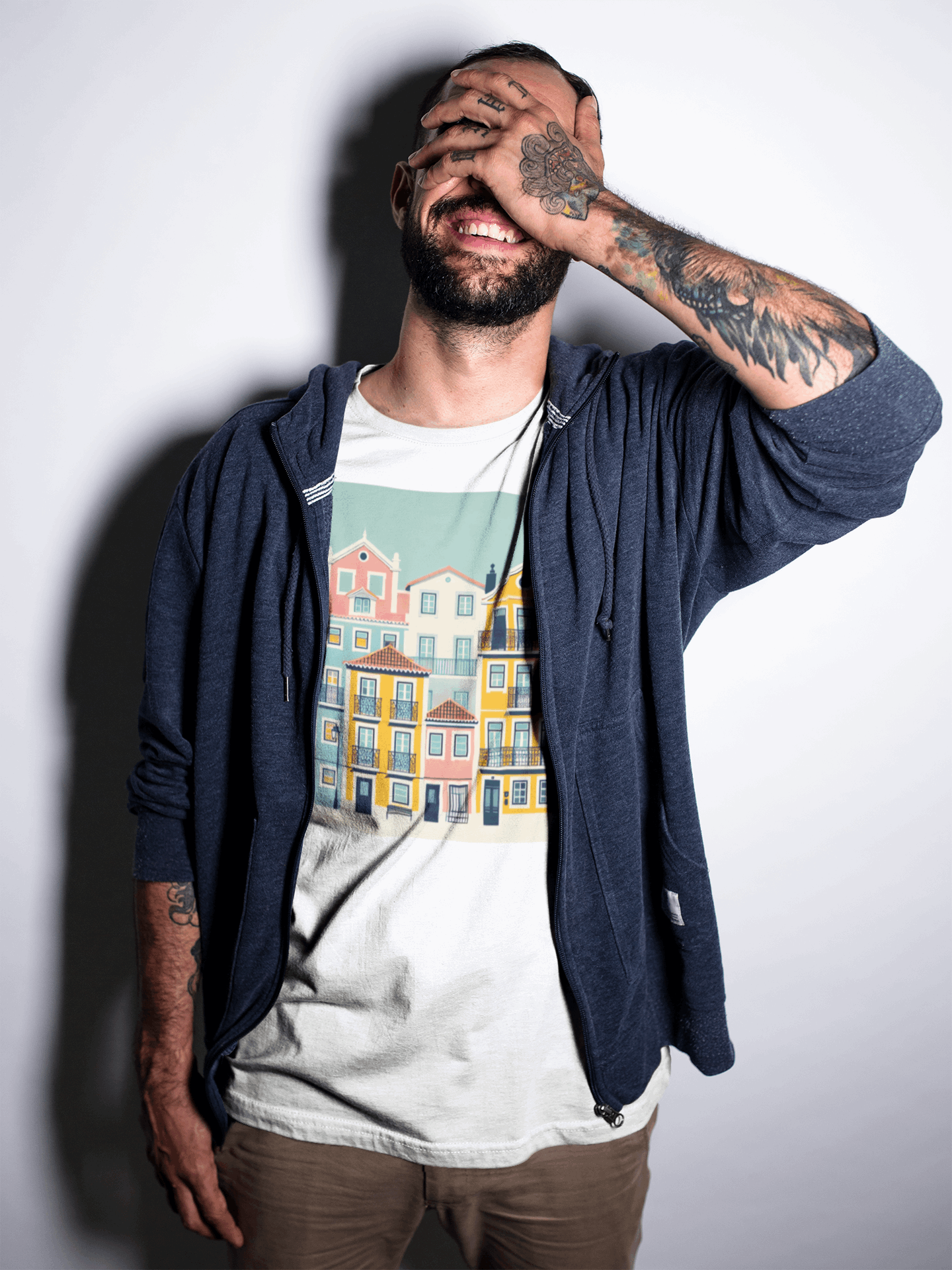 Man in a white unisex T-shirt with Lisbon Alfama houses design, laughing with hand on face. Organic cotton and eco-friendly fashion statement.