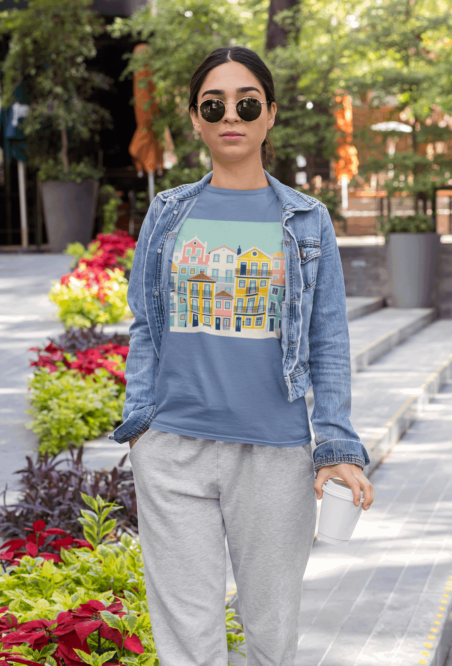Woman in a blue unisex T-shirt with Lisbon Alfama houses print, paired with a denim jacket. Eco-friendly and comfortable for everyday wear.