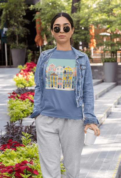 Woman in a blue unisex T-shirt with Lisbon Alfama houses print, paired with a denim jacket. Eco-friendly and comfortable for everyday wear.