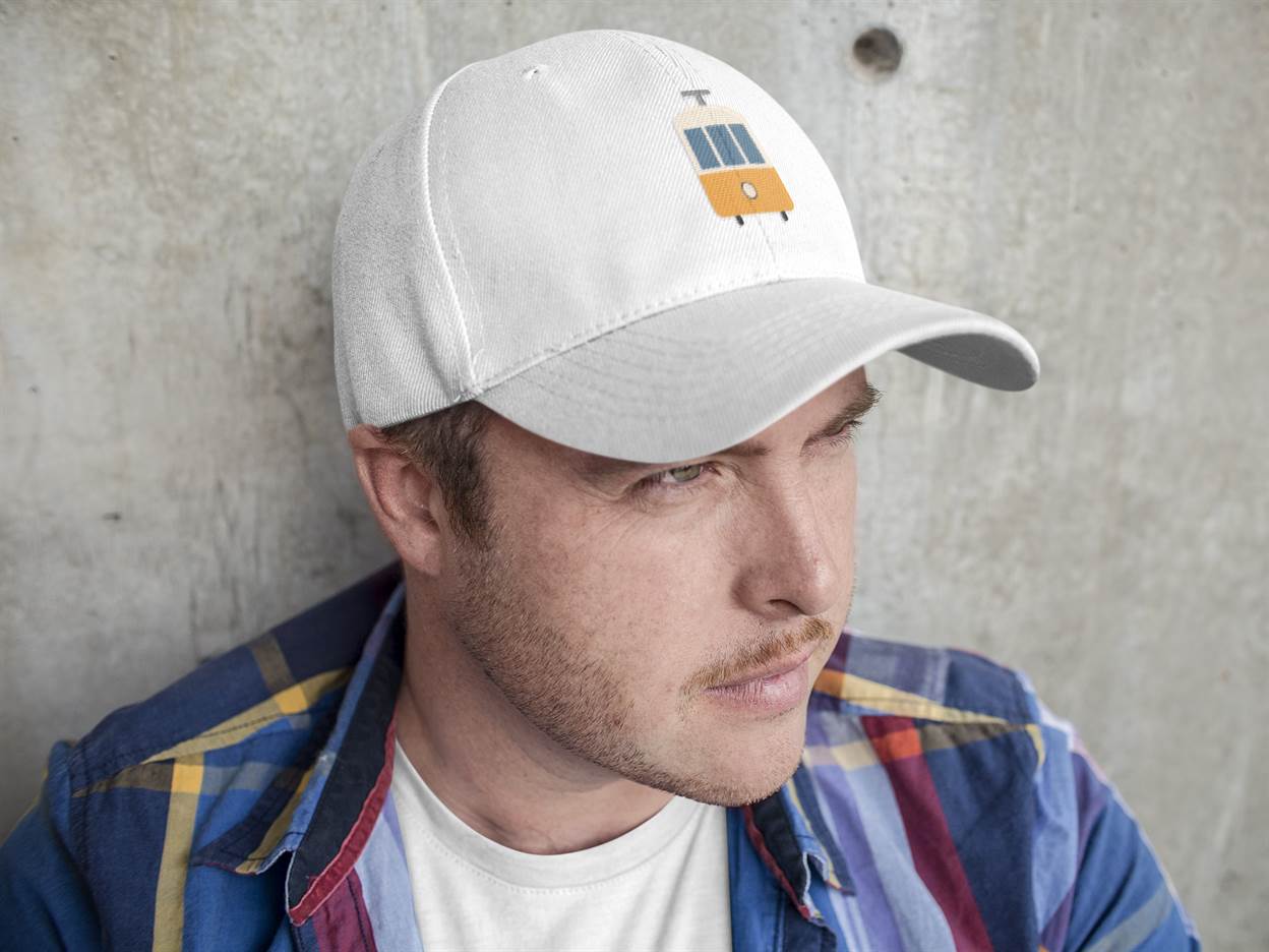 White Lisbon Tram Cap with minimalist embroidery, worn by a man against a concrete wall. A stylish unisex cap celebrating Lisbon's tram heritage.