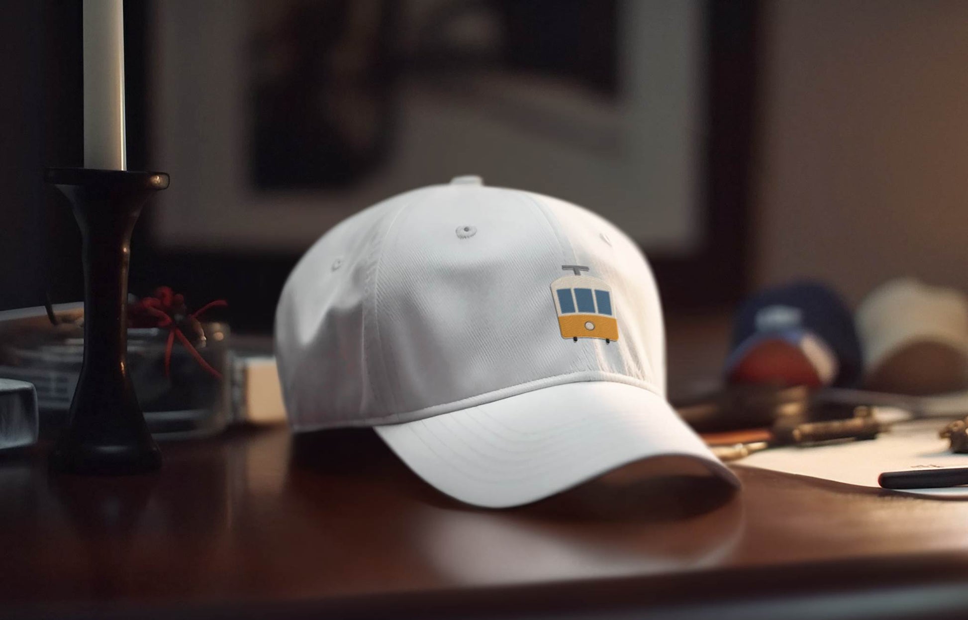 White Lisbon Tram Cap with minimalist embroidered tram logo placed on a wooden desk. A stylish unisex tribute to Lisbon's tram culture.