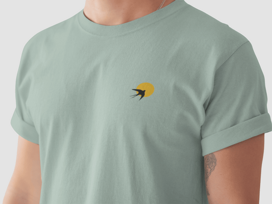 Andorinha T-Shirt in sage green with minimalist swallow logo and yellow sun, crafted from organic cotton for a unisex fit. Inspired by Portugal's heritage.