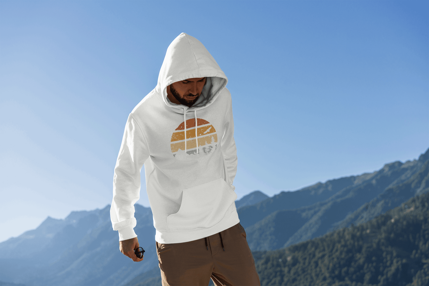 White organic hoodie with a vintage sunset and wildlife design, worn by a man exploring a mountain landscape.