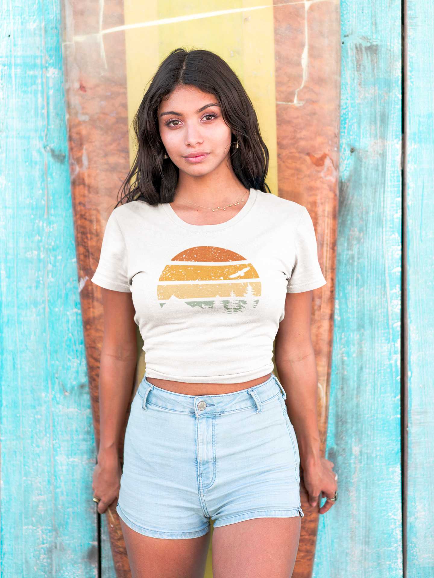 Woman in a cropped white Madeira Mountains Retro Organic Vintage T-Shirt posing by a surfboard. A trendy hiking tee for outdoor lovers.