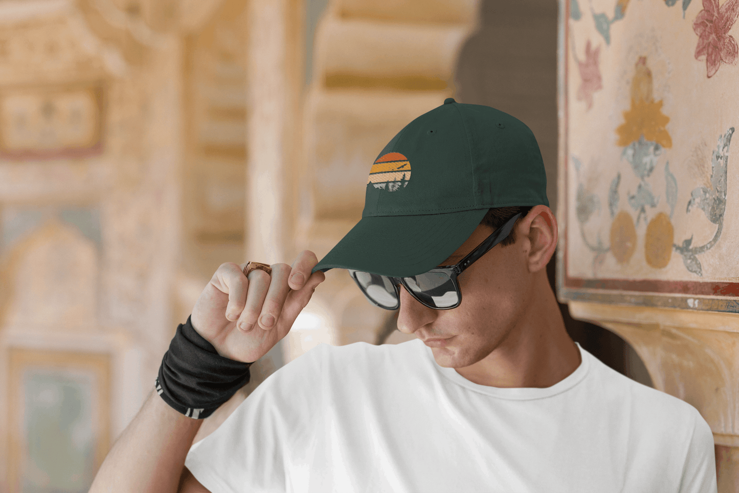 Dark green Madeira Vintage Cap with a mountain logo, worn by a man adjusting it while wearing sunglasses. A stylish and adventurous look.