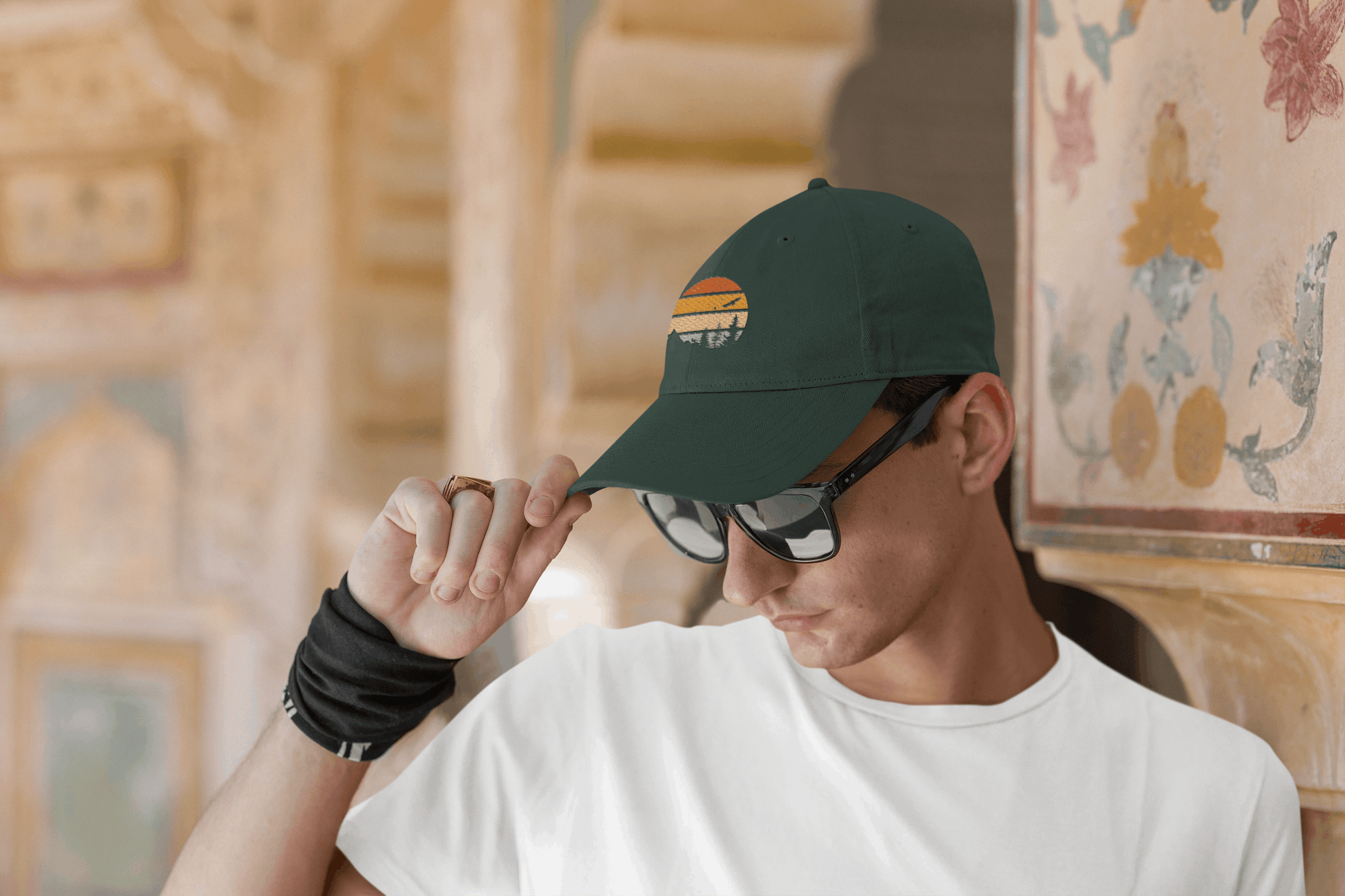 Dark green Madeira Vintage Cap with a mountain logo, worn by a man adjusting it while wearing sunglasses. A stylish and adventurous look.