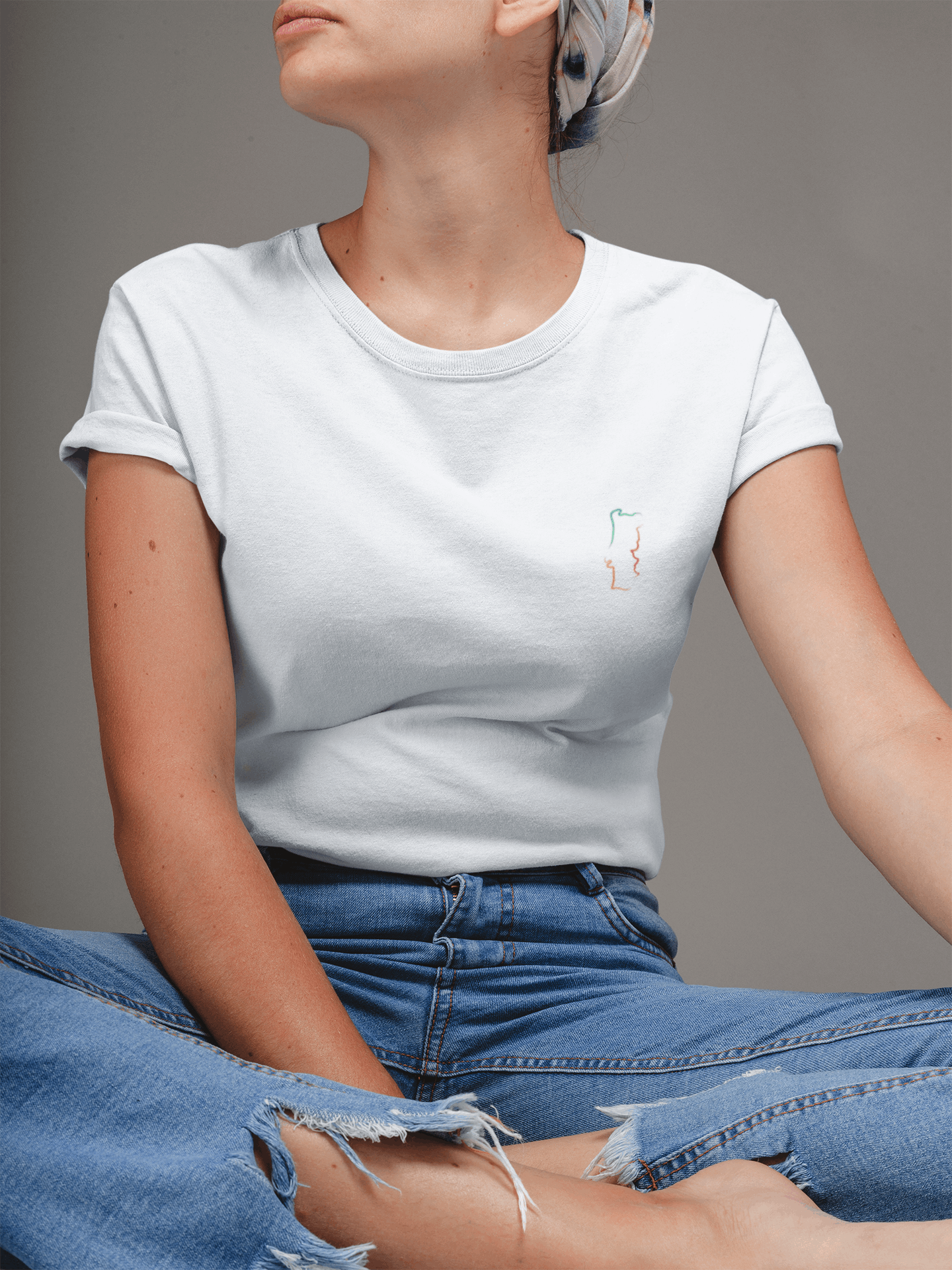 Woman sitting cross-legged in a white Portugal T-Shirt with a minimalist embroidered map design, made from organic cotton for a casual and eco-friendly style.