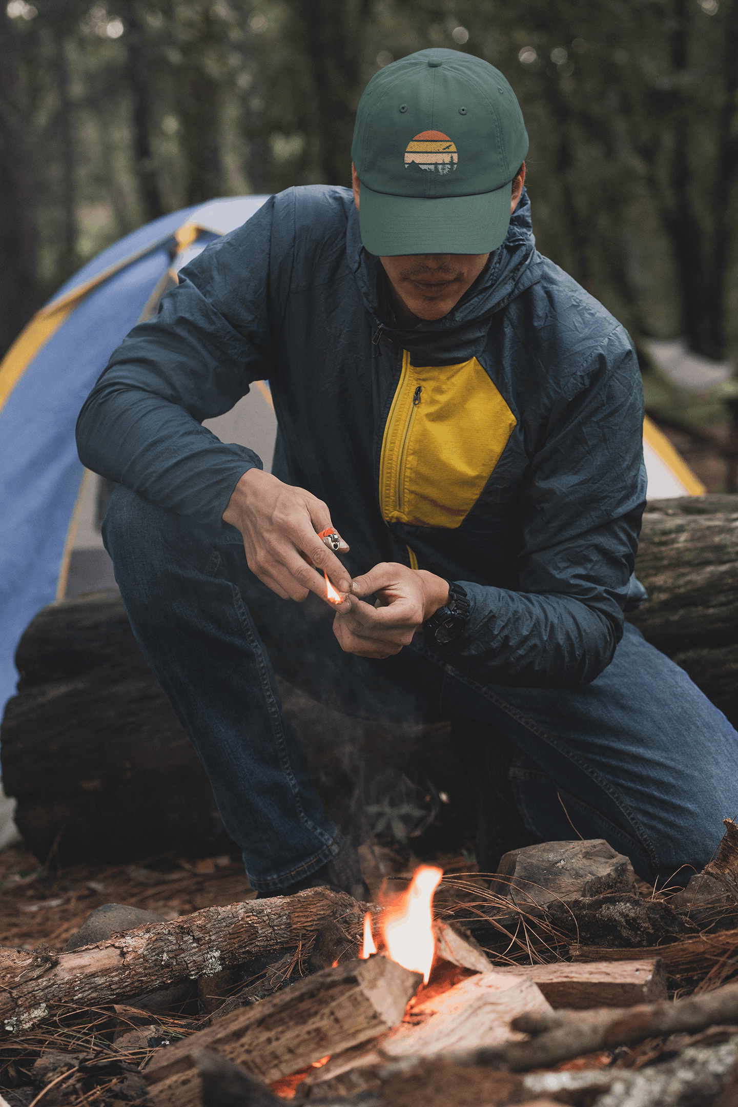 Madeira Vintage Cap in green with a mountain logo, worn by a camper lighting a fire. Perfect for outdoor adventures and rugged exploration.