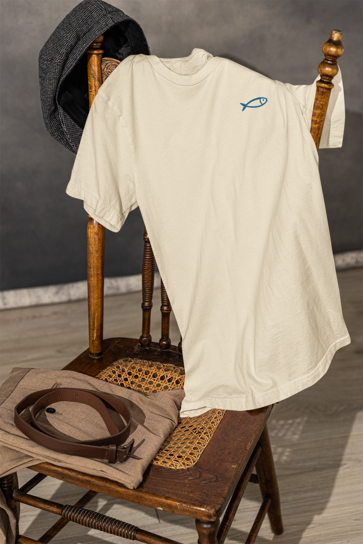 Organic cream crew neck t-shirt with minimalist blue sardine graphic, draped on wooden chair, Portugal gift style.