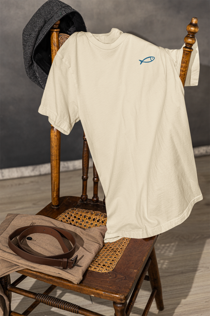 Organic cream crew neck t-shirt with minimalist blue sardine graphic, draped on wooden chair, Portugal gift style.
