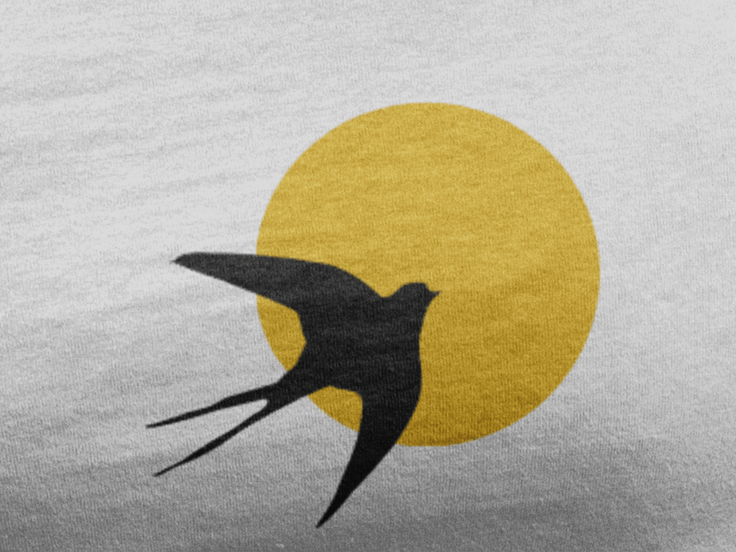Close-up of the Andorinha logo on an organic cotton t-shirt, featuring a black swallow against a yellow sun. A sustainable and cultural fashion statement.