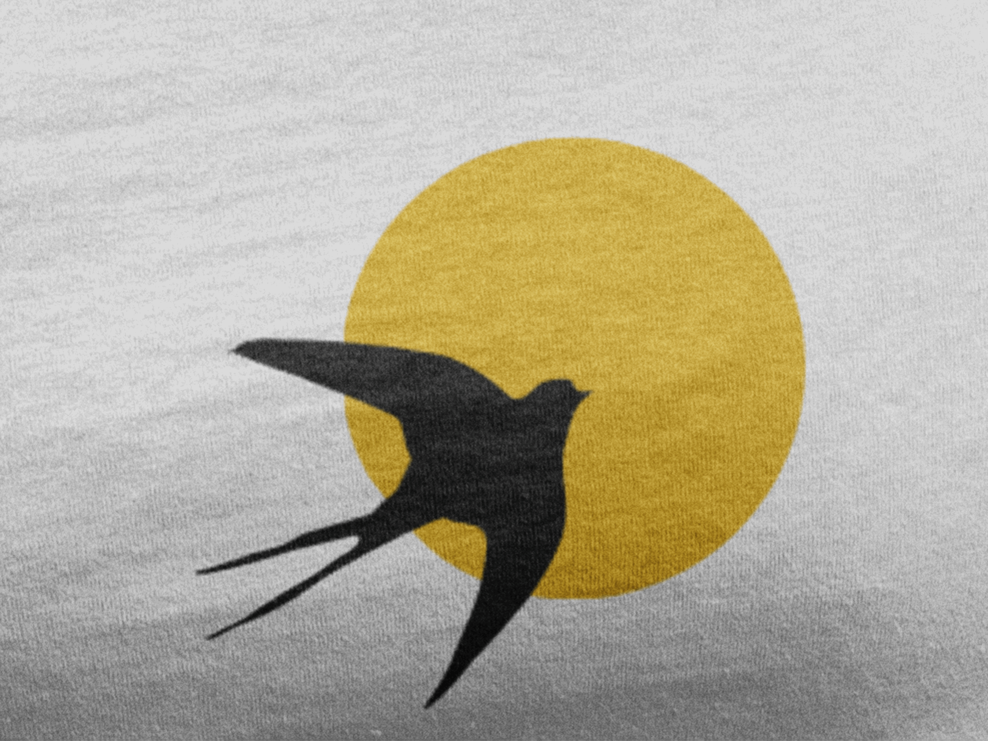 Close-up of the Andorinha logo on an organic cotton t-shirt, featuring a black swallow against a yellow sun. A sustainable and cultural fashion statement.