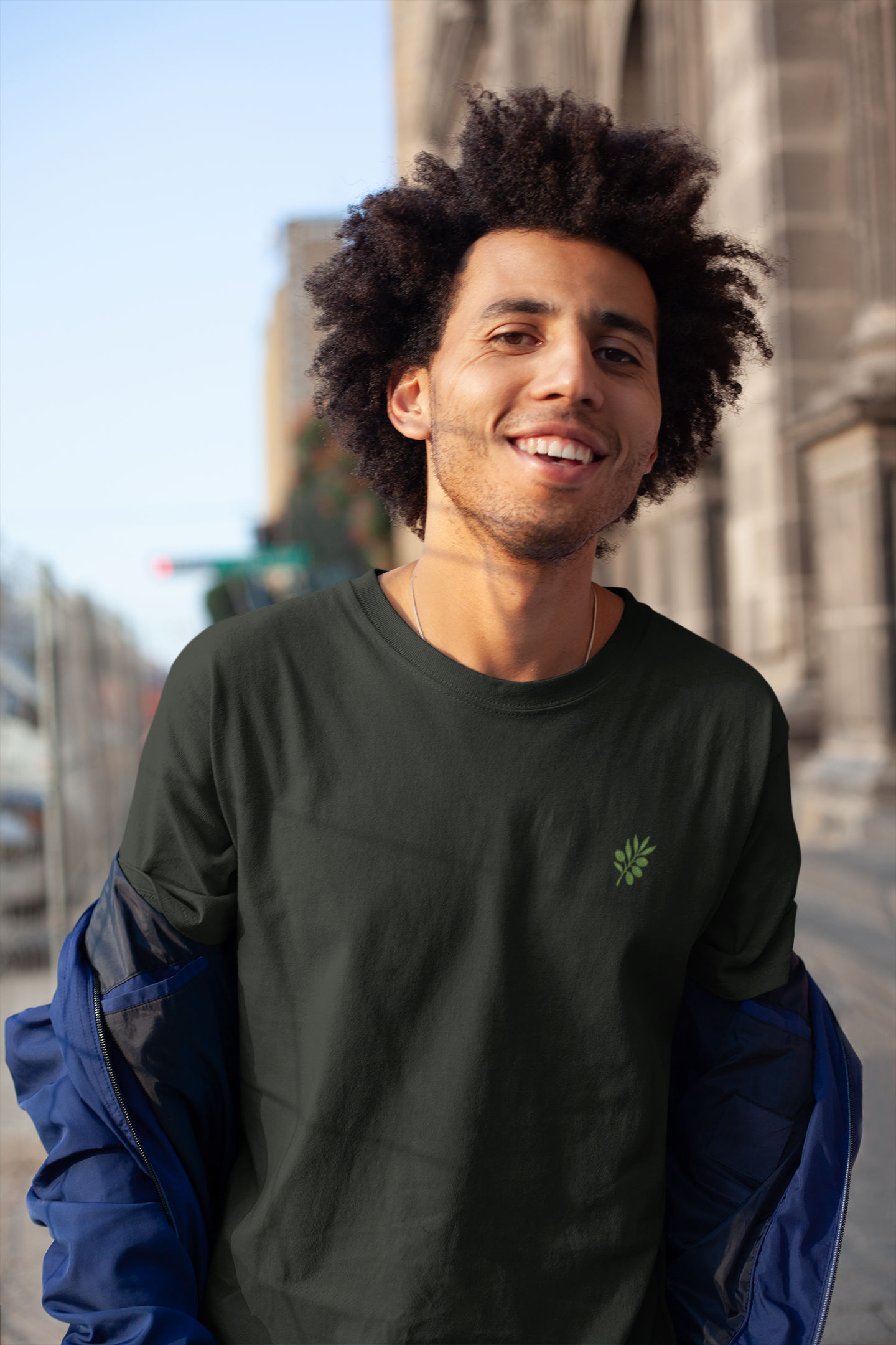 Man wearing a dark green sweatshirt with a logo, standing outdoors with a building in the background.