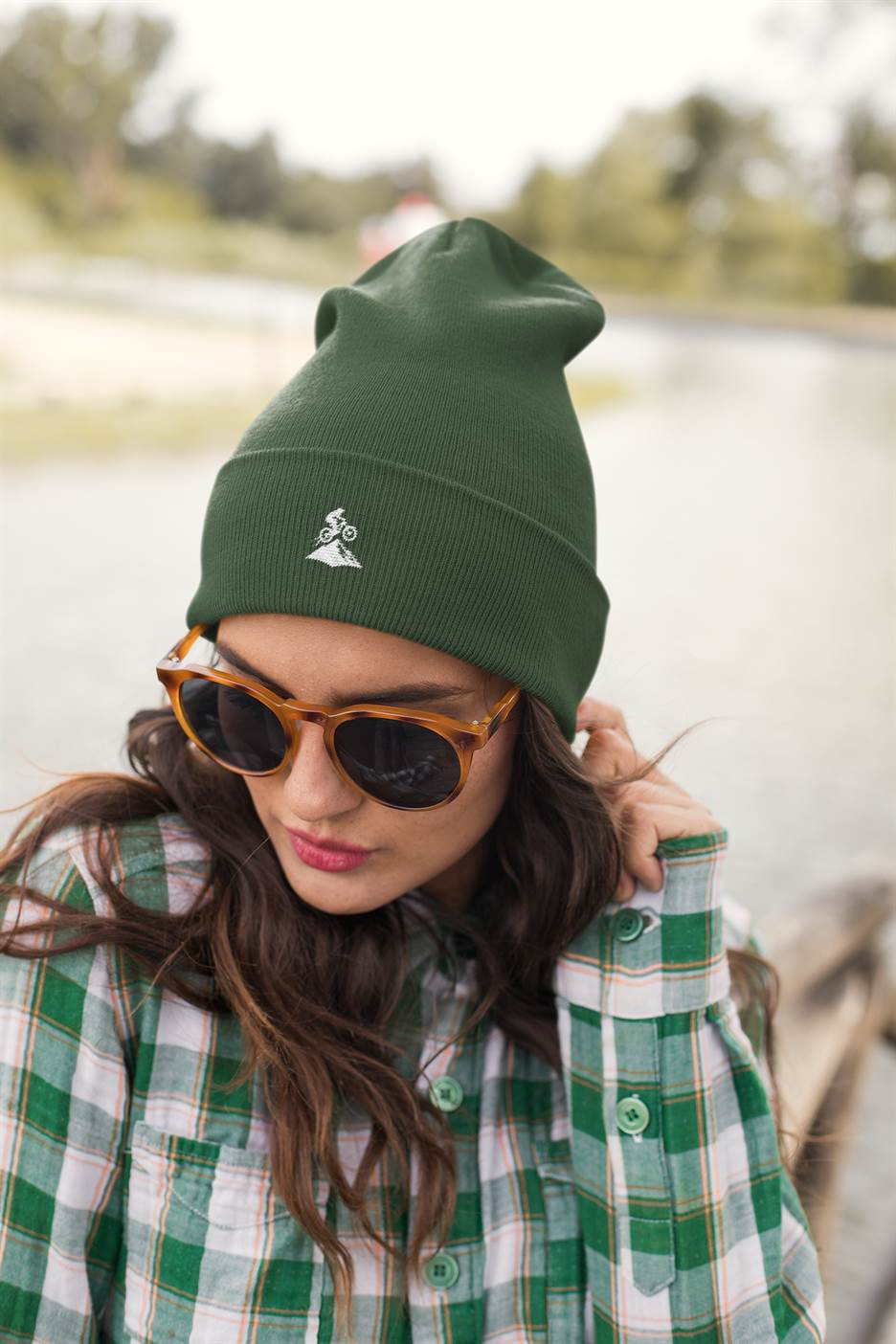 Green Madeira Beanie with embroidered mountain bike logo, worn by a woman with sunglasses. A stylish and functional accessory for outdoor activities.