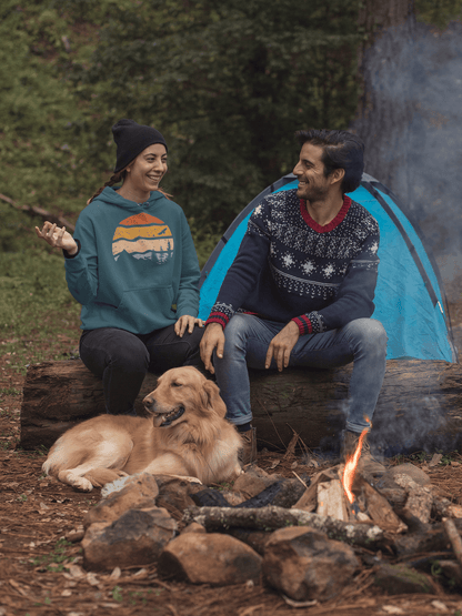 Teal organic cotton hoodie with a retro sunset print, worn by a woman sitting by a campfire with a dog and a companion.