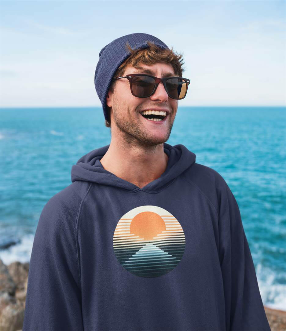Navy blue Nazaré vintage hoodie with a retro sunset graphic, worn by a man near the ocean. A perfect eco-friendly hoodie for surf and casual wear.