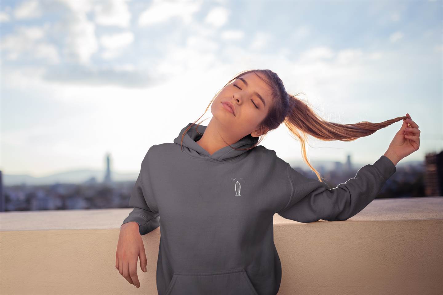 Dark gray Ericeira Surf Hoodie worn on a rooftop at sunset. Organic and unisex, offering comfort and a relaxed surf-inspired look.