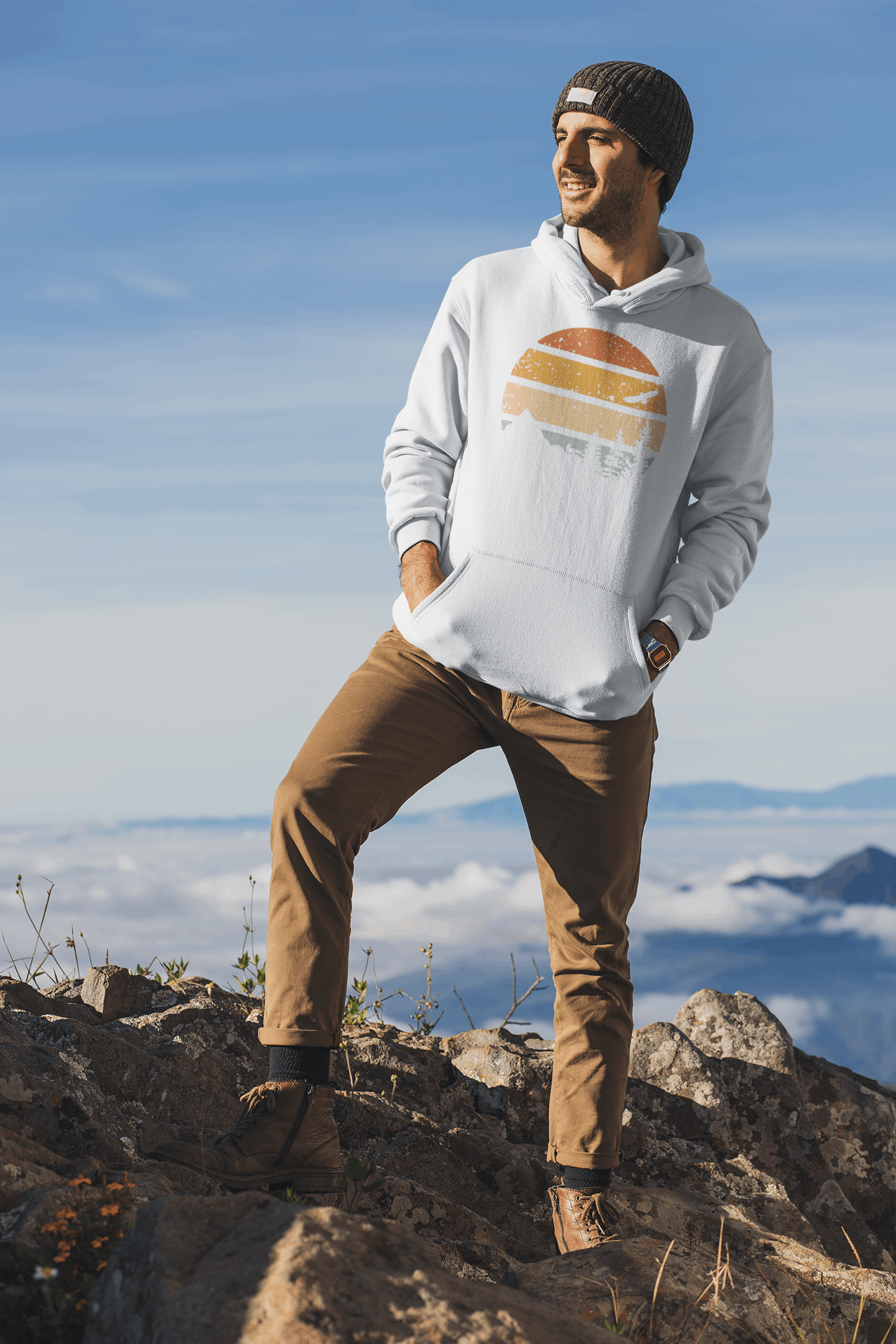 White adventure hoodie with a retro sunset and nature design, worn by a man standing on a rocky peak with a scenic backdrop.