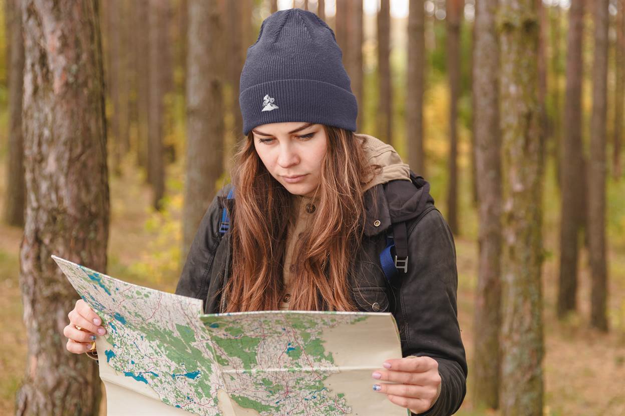 Navy blue Madeira Beanie with embroidered mountain bike logo, worn by a woman reading a map in the woods. Perfect for explorers and bikers.