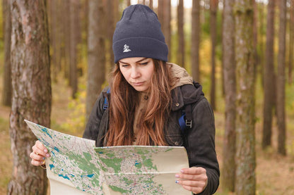 Navy blue Madeira Beanie with embroidered mountain bike logo, worn by a woman reading a map in the woods. Perfect for explorers and bikers.