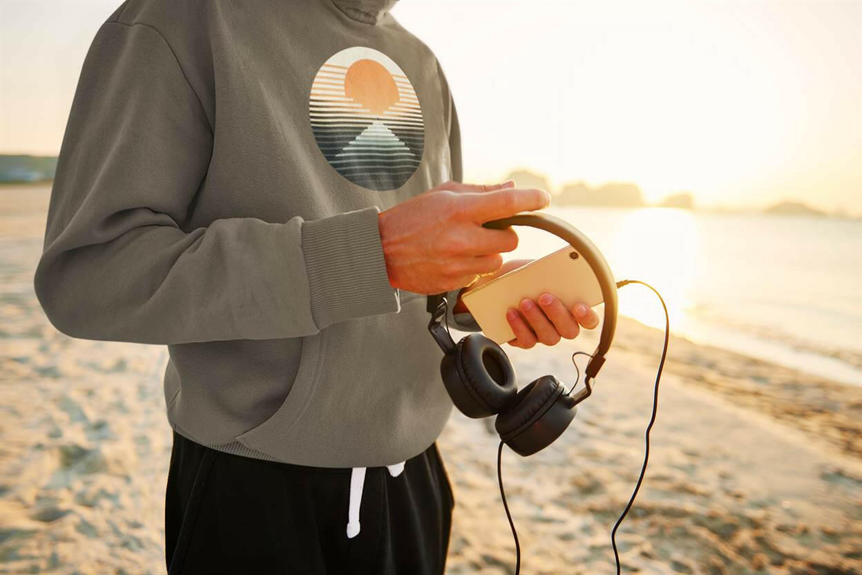 Dark green Nazaré vintage hoodie with a sunset surf graphic, worn on the beach at sunset. Stylish and eco-friendly for casual outdoor wear.