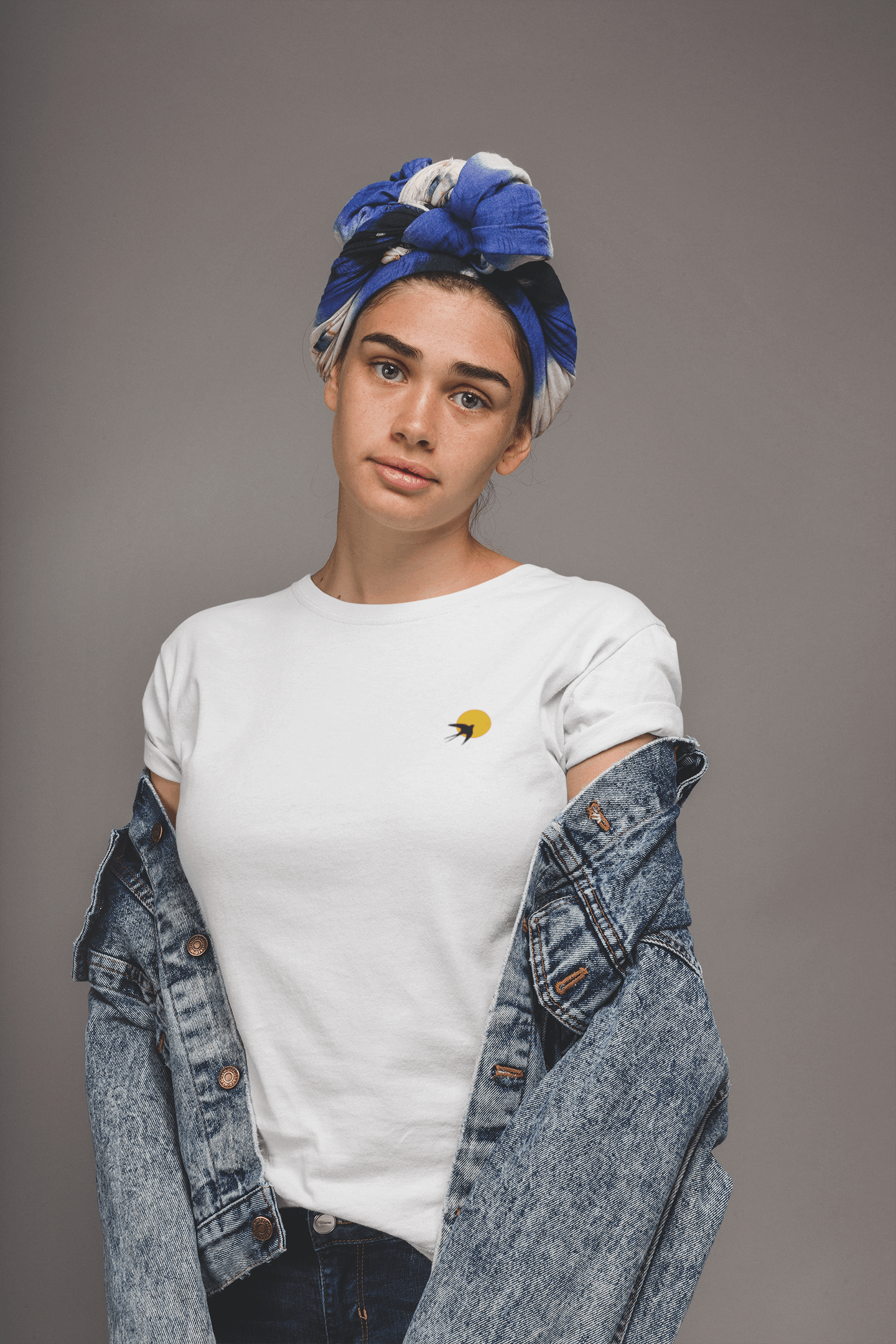 White Andorinha T-Shirt with a small swallow and sun logo, styled with a denim jacket. A unisex organic cotton tee celebrating Portuguese heritage.