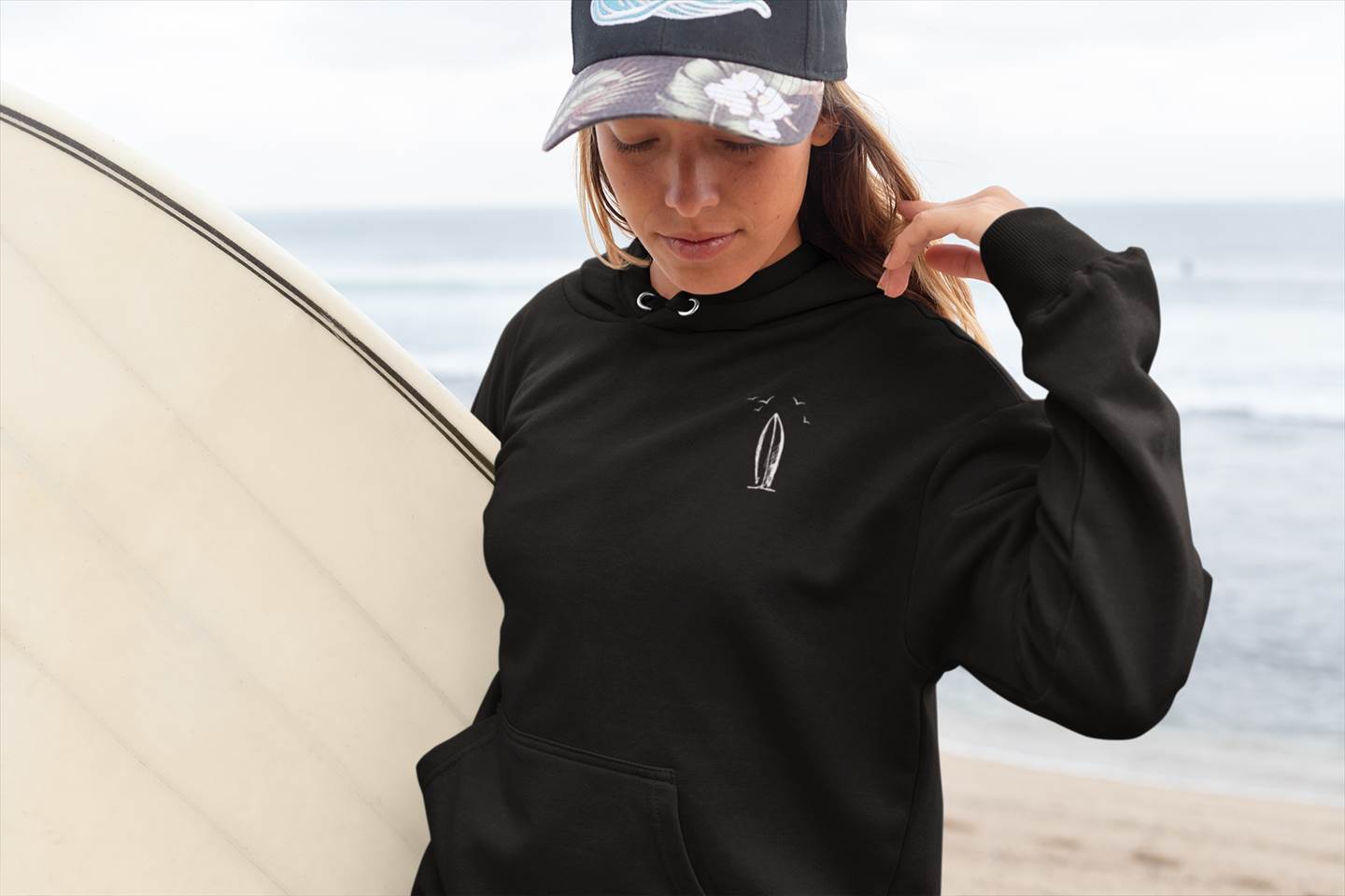 Black Ericeira Surf Hoodie styled with a surfboard. Organic and unisex, blending surf culture with sustainable fashion.