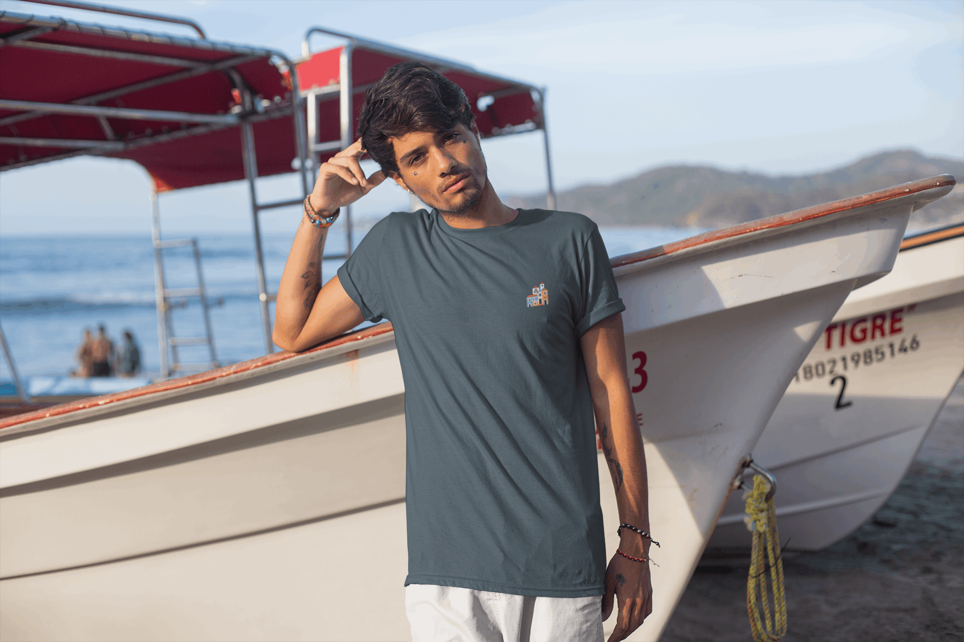 Man in a blue Minimal Alfama Houses Unisex T-Shirt posing by boats, highlighting the breathable organic cotton and minimalist Lisbon design.