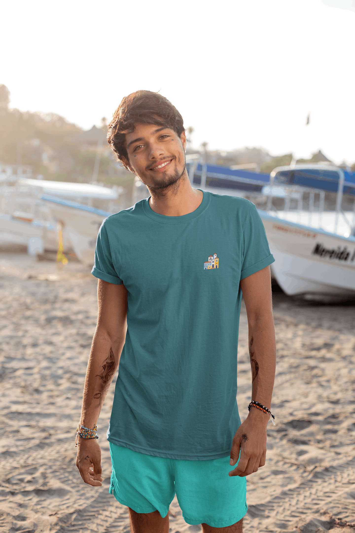 Man in a blue Minimal Alfama Houses Unisex T-Shirt at the beach, styled with turquoise shorts, highlighting the minimalist Lisbon-inspired design.