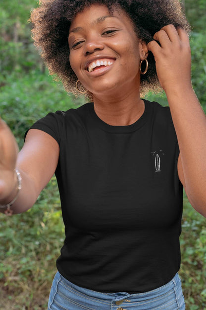 Black Ericeira Surf Organic T-Shirt for women with a minimalist surfboard design, styled casually with jeans for a natural and joyful outdoor look.