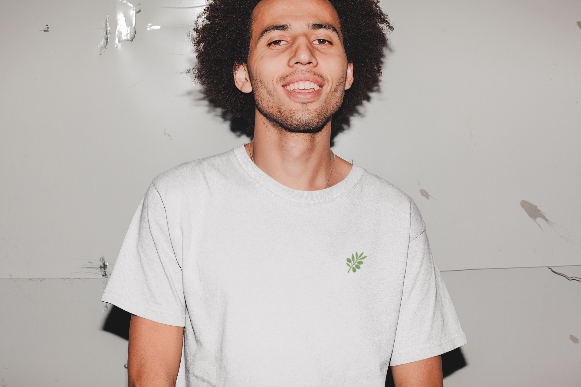 Man wearing a light gray t-shirt with a small green logo against a plain background