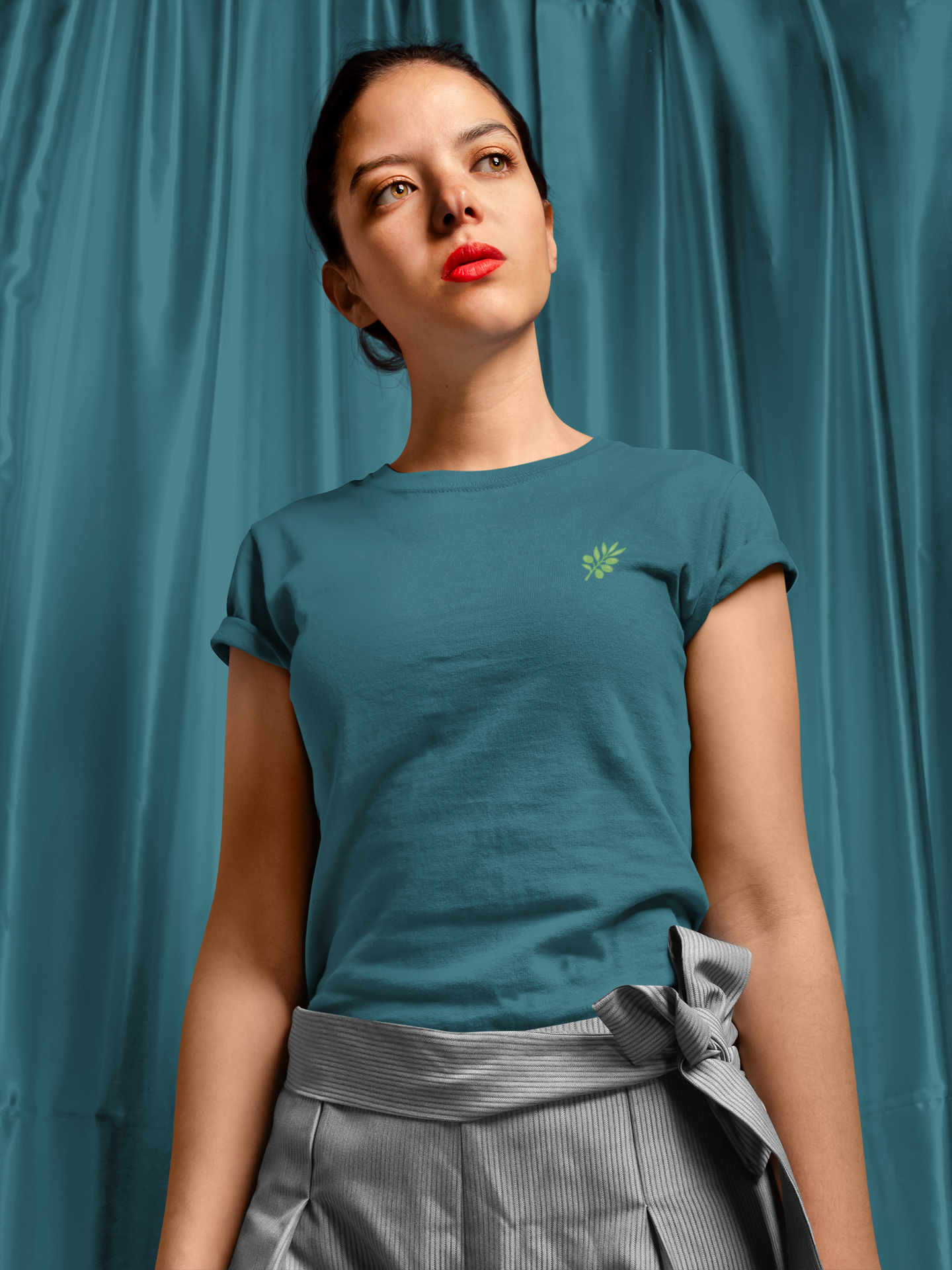 Woman wearing a teal t-shirt with a small logo against a teal curtain background