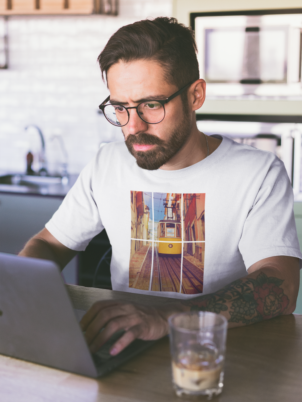 Man in glasses working on a laptop while wearing a Lisbon Tram T-shirt. Made from organic and eco-friendly fabric for a stylish and sustainable look.