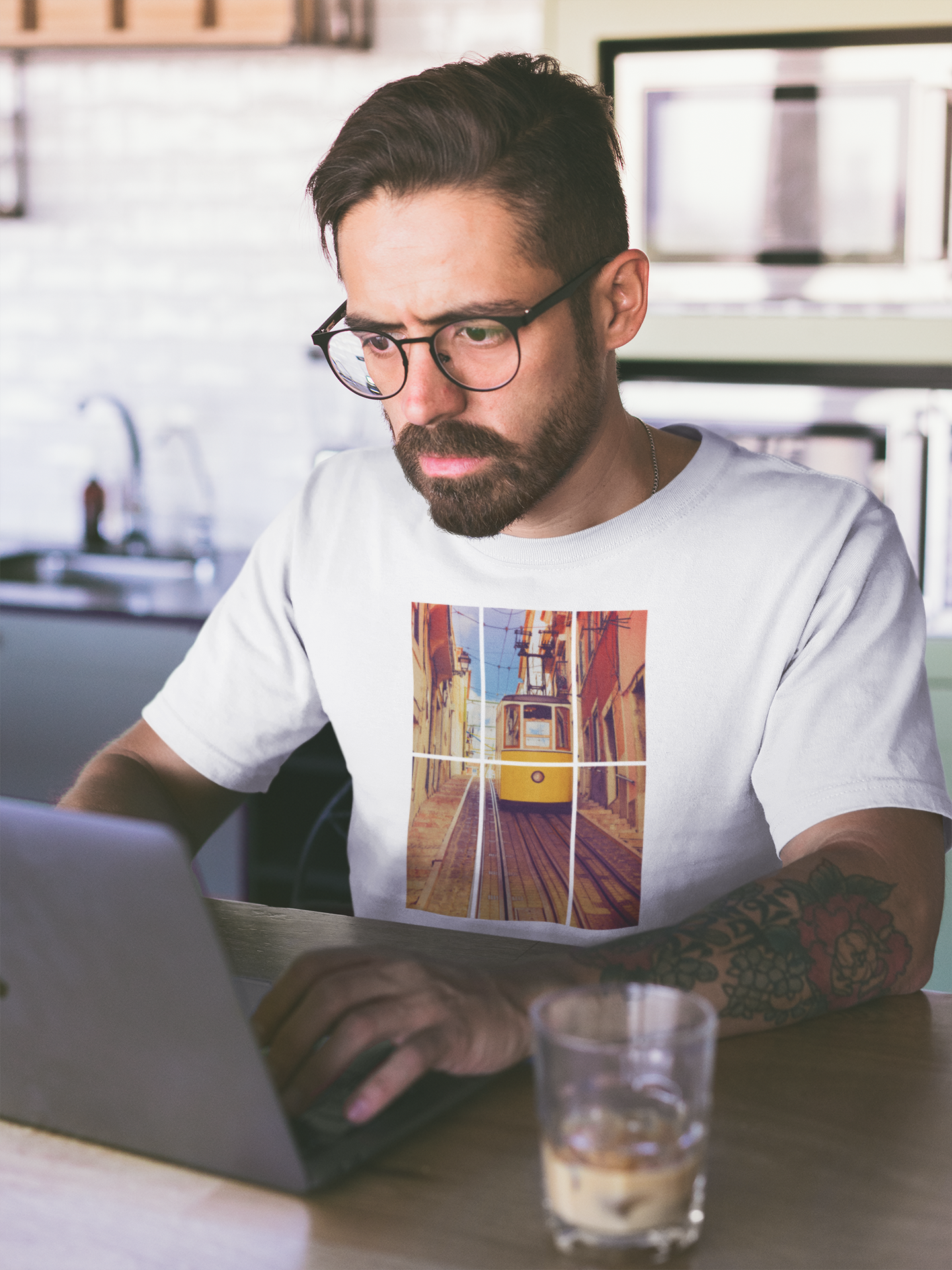 Man in glasses working on a laptop while wearing a Lisbon Tram T-shirt. Made from organic and eco-friendly fabric for a stylish and sustainable look.