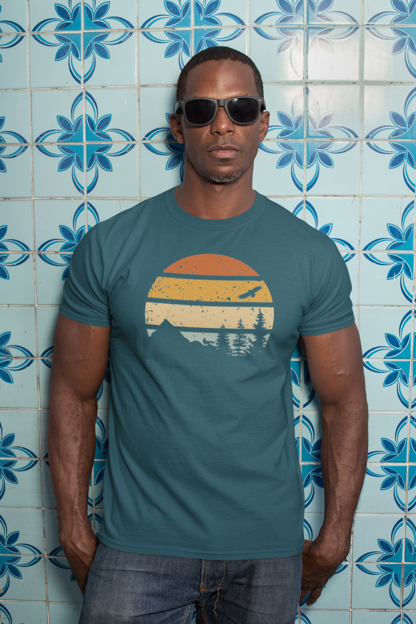 Man wearing a teal Madeira Mountains Retro Organic Vintage T-Shirt against a blue tile background. A rugged hiking tee for adventurers.