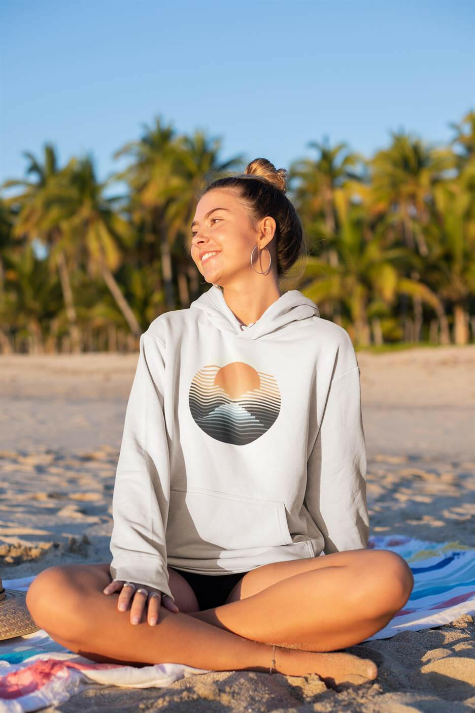 Light-colored Nazaré vintage hoodie with a sunset surf design, worn by a woman on a tropical beach. Sustainable and stylish for outdoor adventures.