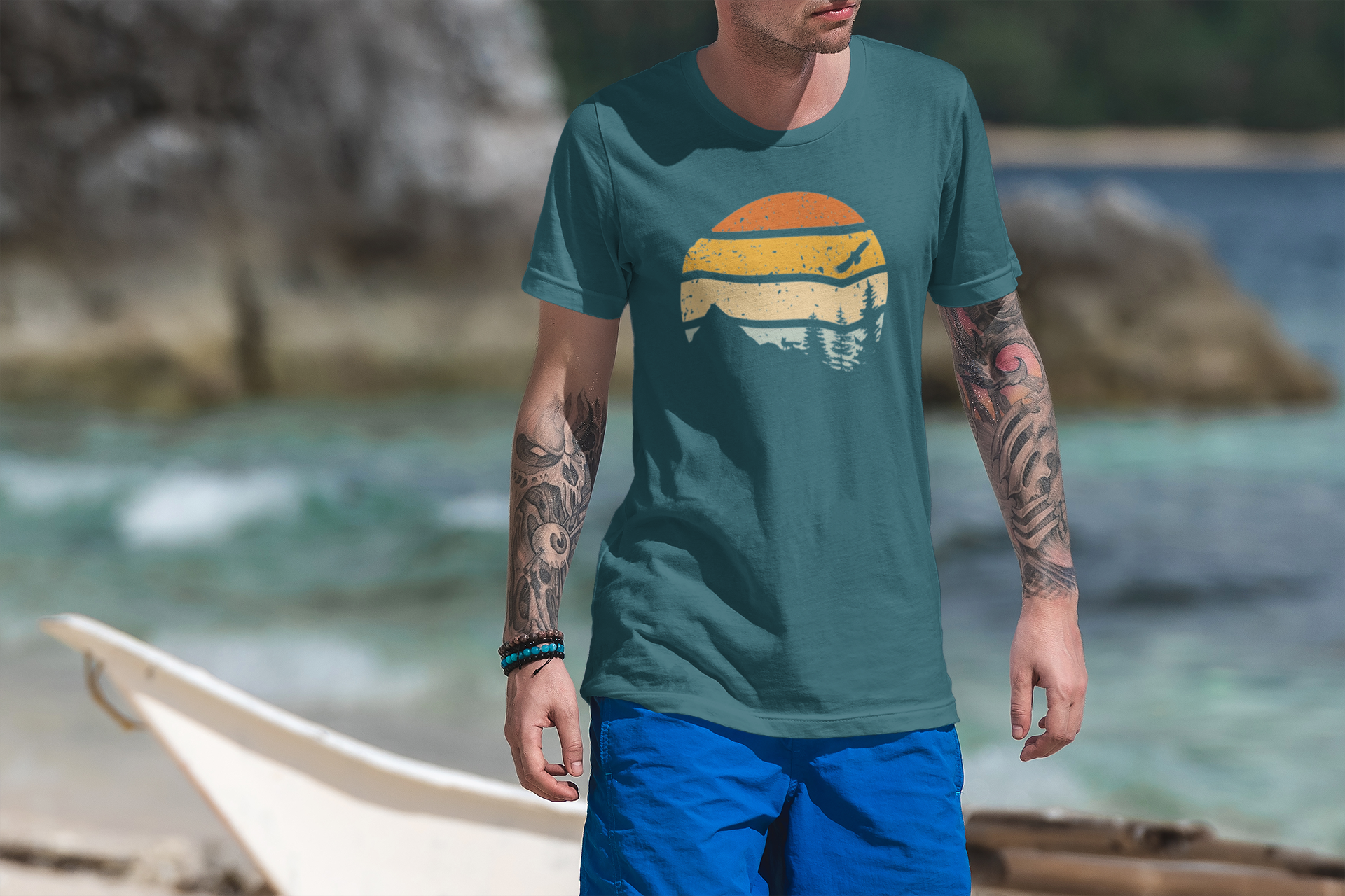 Tattooed man walking by the ocean in a teal Madeira Mountains Retro Organic Vintage T-Shirt. A stylish and comfortable hiking tee.