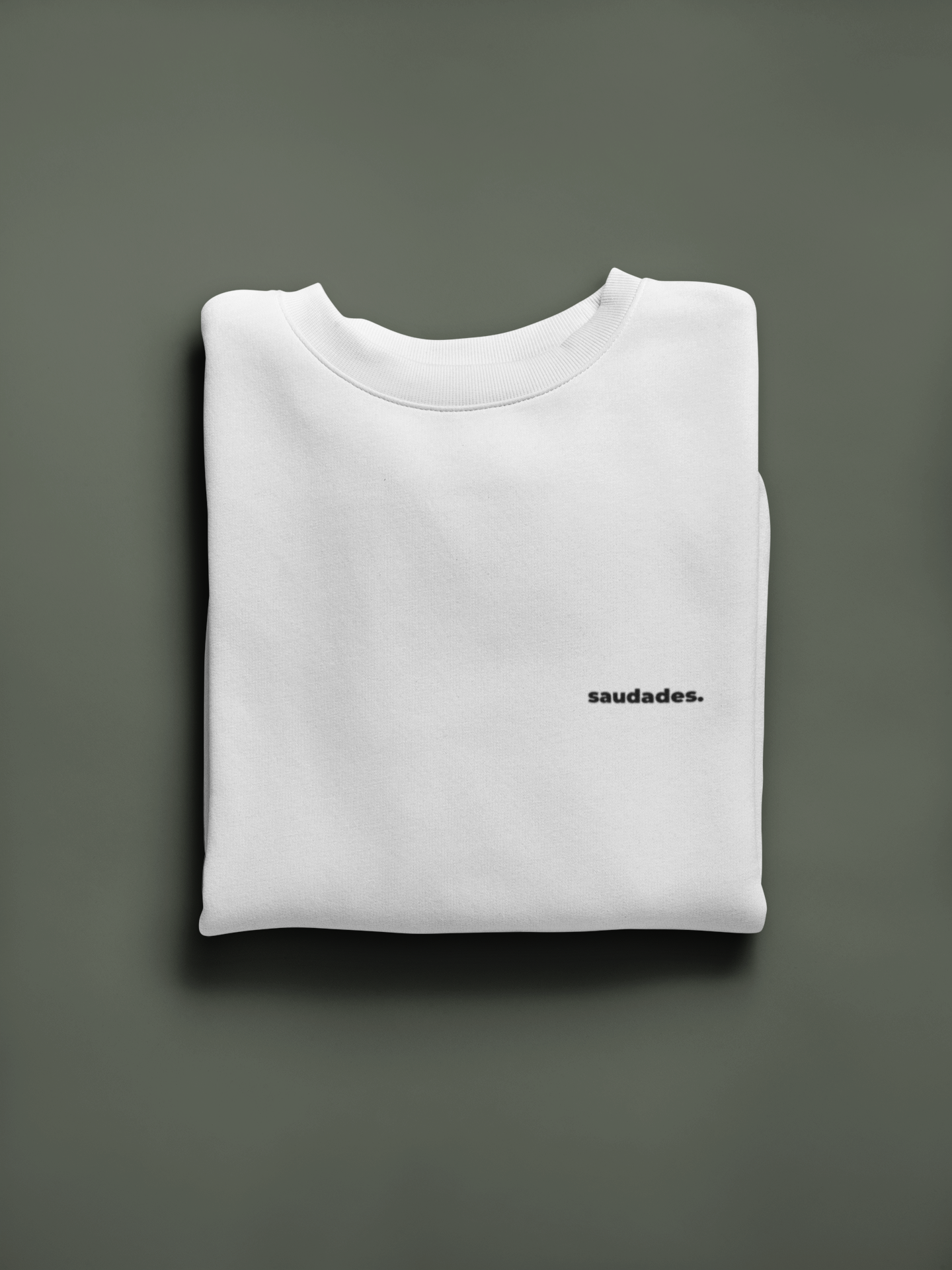 Folded white sweatshirt with 'saudades.' text on a gray background
