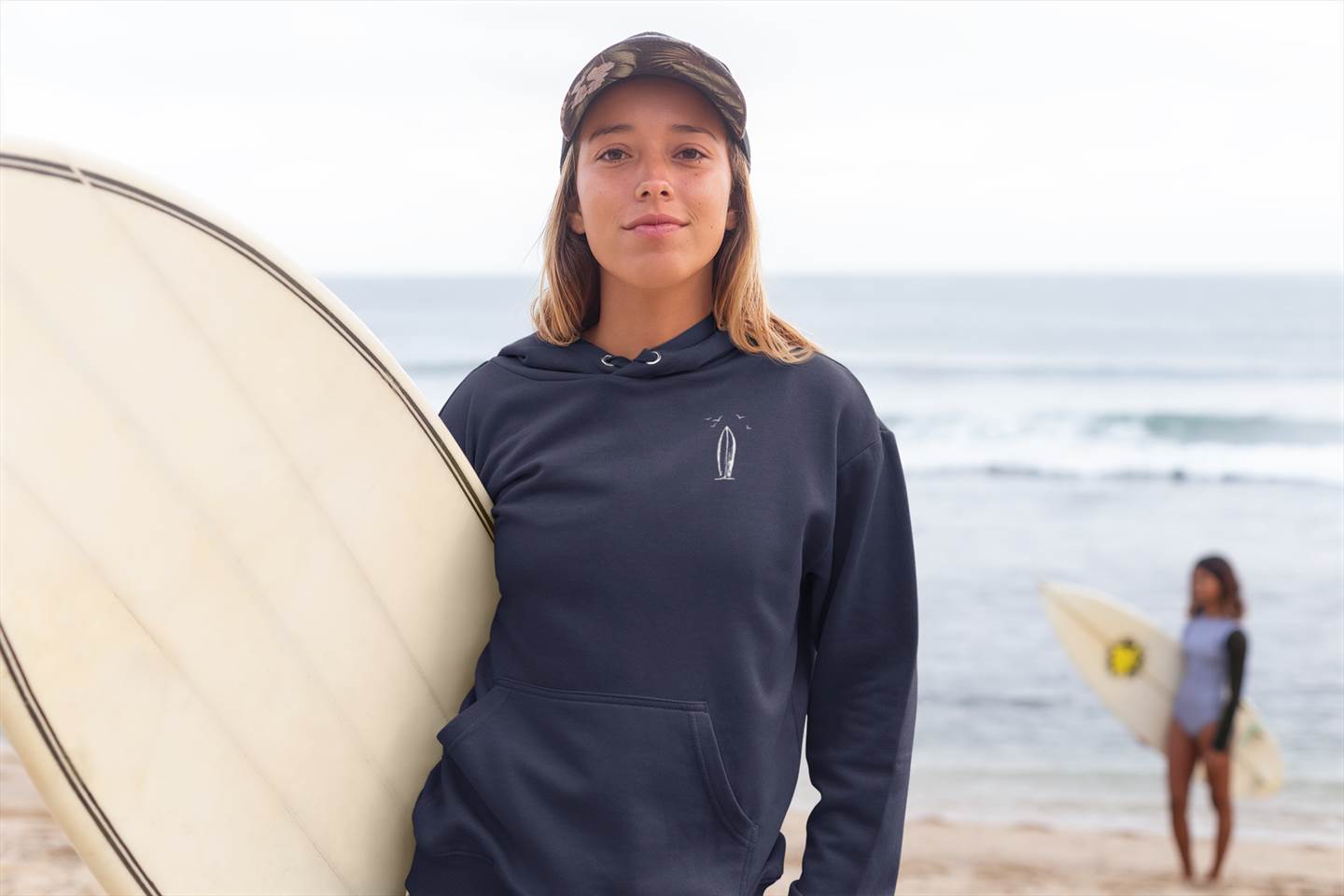 Navy blue Ericeira Surf Hoodie worn by a surfer on the beach. Ethically made, organic, and designed for comfort and style.